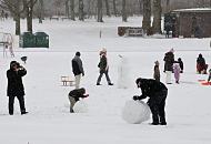 70_5017 Dichter Schnee fllt in Hamburg - im Becken des Planschbeckens, in dem im Sommer die Kinder im Wasser toben, baut ein Vater zusammen mit seinem Sohn einen groen Schneemann; die Mutter fotografiert die Aktion - andere Kinder spielen mit ihren Schlitten. Winterimpressionen von Hamburg - Vater mit Kind baut einen Schneemann.