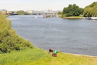 01131_2626 Blick ber die Einfahrt zur Billwerder Bucht zu den Norderelbbrcken - Angler sitzen am Wasser, ein Sportboot in Fahrt Richtung Sperrwerk. Rechts die Halbinsel Entenwerder, Arbeitsboote liegen an Pontons und Wasserbrcken.