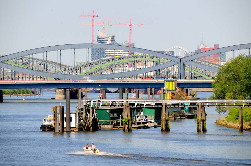 01132_2634 JEhemaliger Zollanleger, Liegeplatz der Zollschiffe in Hamburg Rothenburgsort / Entenwerder; Holzgebäude auf den Pontons - Arbeitsschiffe. Eine Wassertreppe verbindet die Anlage mit dem Ufer von Entenwerder; im Hintergrund die Norderelbbrücke und die Freihafenelbbrücke, die die Zollgrenze zum Hamburger Freihafengebiet bildete.