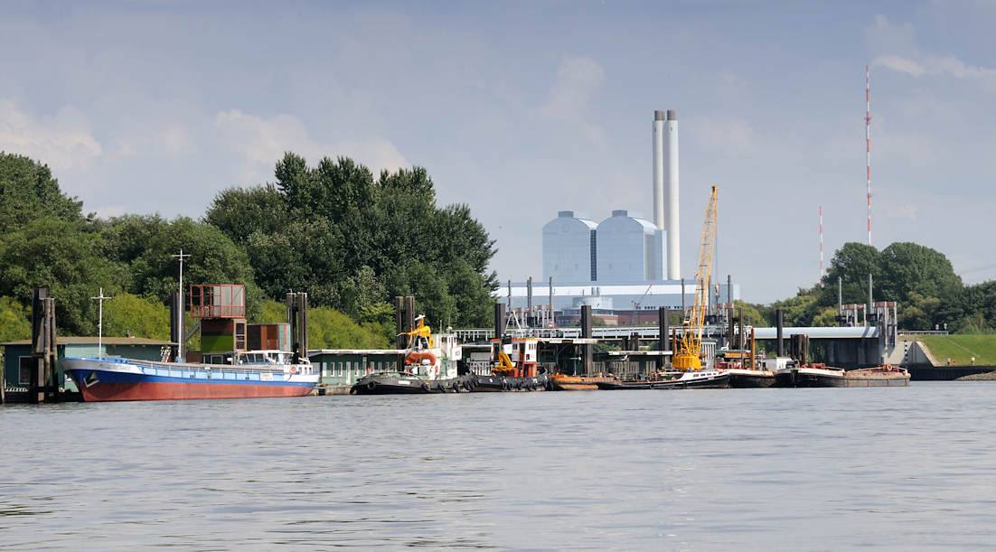 01135_6713 Arbeitsschiffe am Anleger Entenwerder, Hamburg Rothenburgsort / Norderelbe; am Ponton haben ein Binnenschiff und mehrere Schlepper festgemacht - ein Schwimmkran liegt zwischen mehreren Schuten. Dahinter die Tore vom Sperrwerk Billwerder Bucht und die hohen Gebäude und Schornsteine vom Heizkraftwerk Tiefstack.