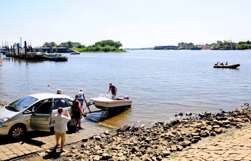 01172_2689 ffentliche Slipanlage in Entenwerder an der Norderelbe in Hamburg Rothenburgsort; ein kleines Sportboot wird von einem Bootstrailer zu Wasser gelassen. Im Hintergrund lks. die Bootstankstelle / Bunkerboot vor dem Sperrwerk Billwerder Bucht und re. das Ufer der Peute in Hamburg Veddel.