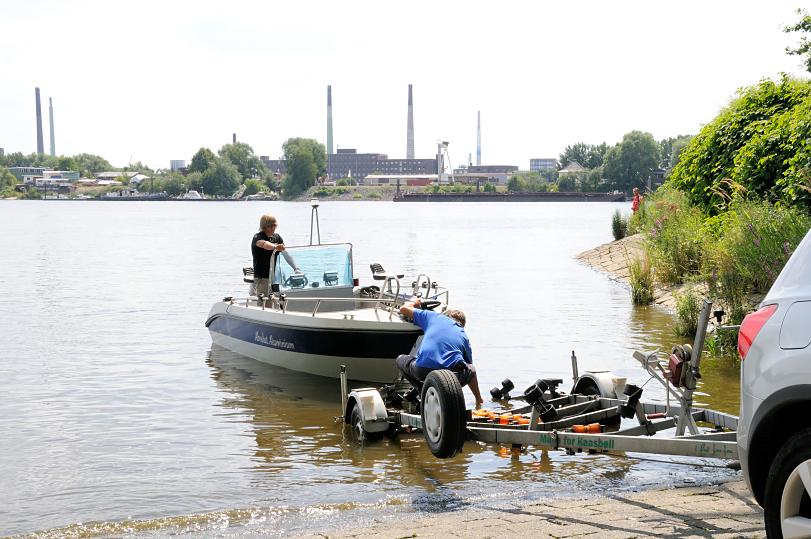 01173_3703 Ein Sportboot wird von einem Trailer auf der Slipanlage im Elbpark Entenwerder zu Wasser gelassen - auf der anderen Seite der Norderelbe Industrieschornsteine und Gebäude auf der Peute in Hamburg Veddel.