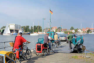 3897 Autofhre / Personenfhre - Seilfhre ber die Schlei bei Arnis, Schleswig Holstein. Fahrradfahrer mit Anhnger fahren auf die Seilfhre ber die Schlei - im Hintergrund die Stadt Arnis.