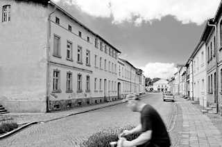 7655 Einstckige Wohnblocks, Etagenwohnungen im Hansensgang von Pritzwalk - Fahrradfahrer in Fahrt, Schwarz-Weiss-Fotografie.