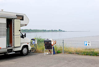 1525 Stellpltze fr Wohnmobile am Hafen Glcksstadt - eine Besucherin der Stadt sitzt neben ihrem Wagen im Campingstul und liest die Zeitung - im Hintergrund die Einfahrt zur Unterelbe.