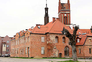 0114 Altes Rathaus von Mehlsack / Pieniężno, Polen. Das Backsteingebude steht leer, die Fenster sind vernagelt - Kirchturm der katholischen Kirche der Stadt.