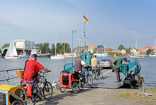 3897 Autofähre / Personenfähre - Seilfähre über die Schlei bei Arnis, Schleswig Holstein. Fahrradfahrer mit Anhänger fahren auf die Seilfähre über die Schlei - im Hintergrund die Stadt Arnis.
