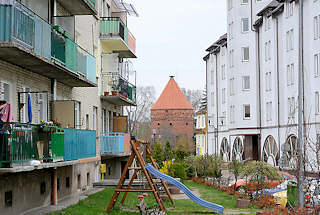 0230 Mehrstckige Wohnhuser mit farbigen Balkons - Wiese mit Kinderspielplatz; im Hintergrund der sogen. Storchenturm, Teil der Befestigungsanlage von Dobre Miasto / Guttstadt, Polen.