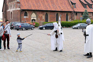 5108 Hof der Ordensburg in Malbork / Marienburg, Polen. Als Ordensritter verkleidete Mnner spielen mit einem Kind Schwertkampf.
