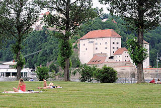 3130 Wiese auf der Landspitze an der die Inn in die Donau mndet - Menschen liegen auf Decken in der Sonne - am gegenberliegenden Donauufer die Veste Niederhaus an der die Ilz in die Donau fliesst. 