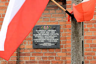 0013 Gedenktafel BERNARD SYCHTA in Pelplin, Polen - polnische Flaggen, weiss-rot. Bernard Sychta war Pfarrer an der Kathedrale von Pelplin und schrieb ein Kompendium ber die Kultur der Kaschuben.