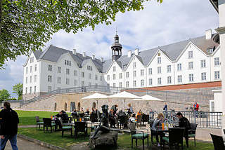 1856 Aussengastronomie, Tische mit Gsten und Sonnenschirmen vor dem Plner Schloss; das Schloss ist eines der grten Schlsser Schleswig-Holsteins, errichtet im 17. Jahrundert - Residenz der Herzge von Pln; jetzt in Privatbesitz / gemeinntzige Stiftung, Akademie.