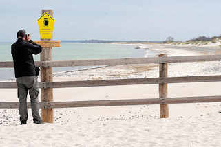 11_8604 Holzzaun, Abgrenzung am Strand auf der Halbinsel Zingst - Hinweisschild Nationalpark Vorpommersche Boddenlandschaft, Kernzone - Brut-, Rast- und berwinterungsgebiet - Betreten verboten. Ein Fotograf fotografiert das Schild.